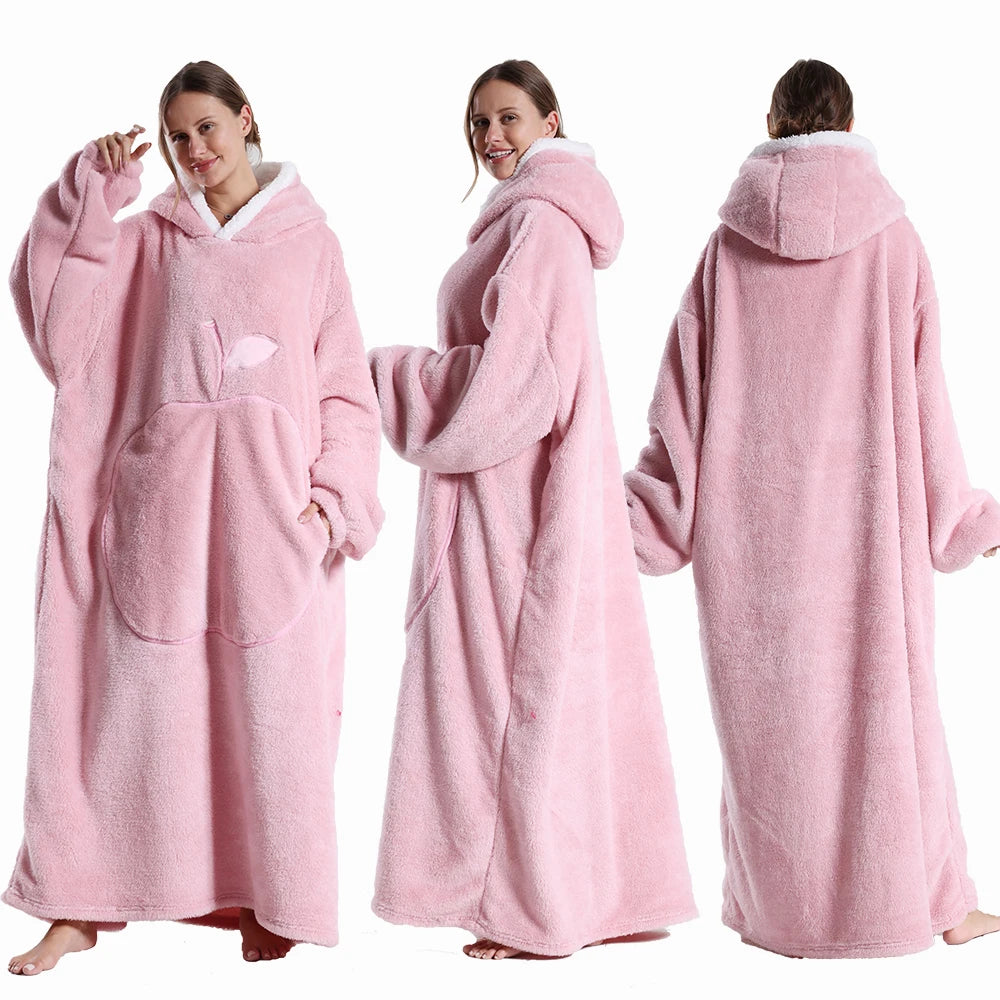 Deux vues d’une couverture-hoodie oversize rose en sherpa portée par une femme ; capuche doublée blanche et grande poche kangourou visible.